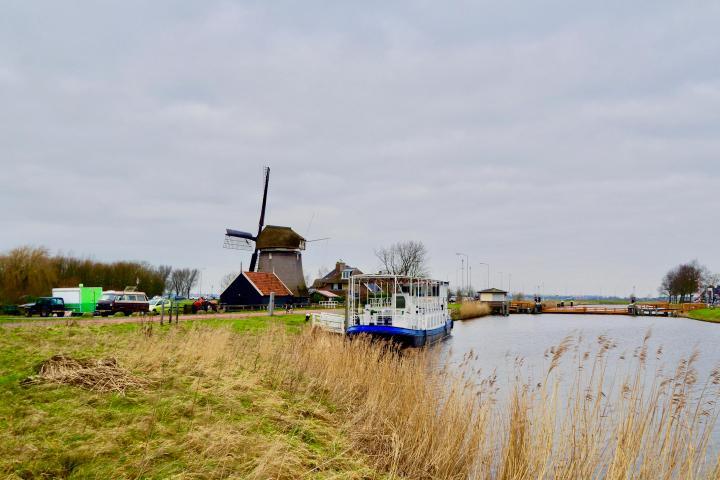 View of the boat on a river next to a big windmill