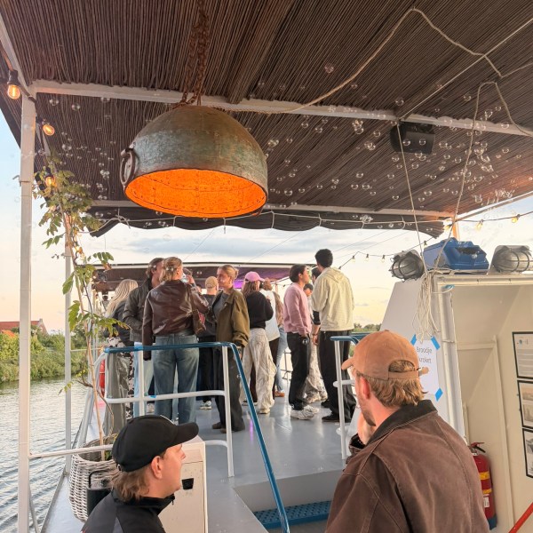 People socializing on a boat deck with a large metal light fixture overhead.