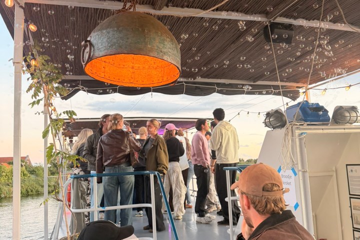 People socializing on a boat deck with a large metal light fixture overhead.