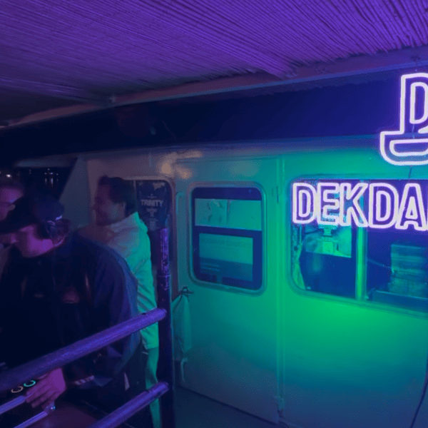 DJ performing on a dimly lit stage with neon 'DEKDANSEN' sign.