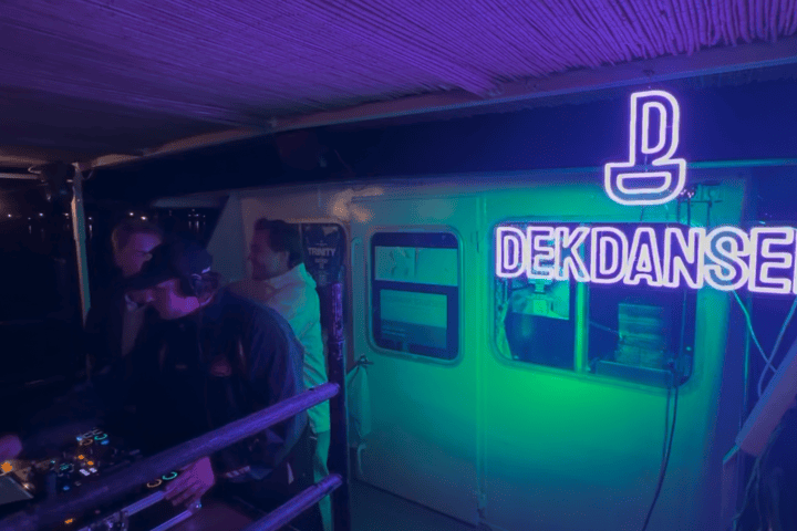 DJ performing on a dimly lit stage with neon 'DEKDANSEN' sign.