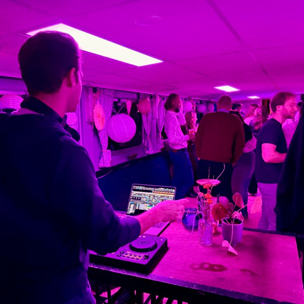 DJ playing music at a pink-lit party on a boat with people dancing.