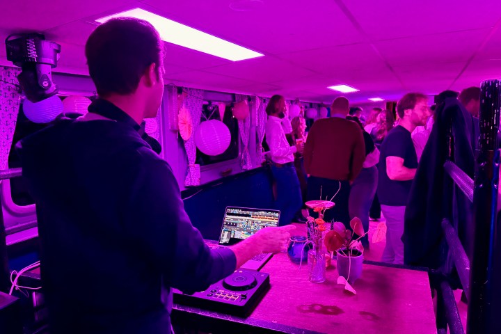 DJ playing music at a pink-lit party on a boat with people dancing.