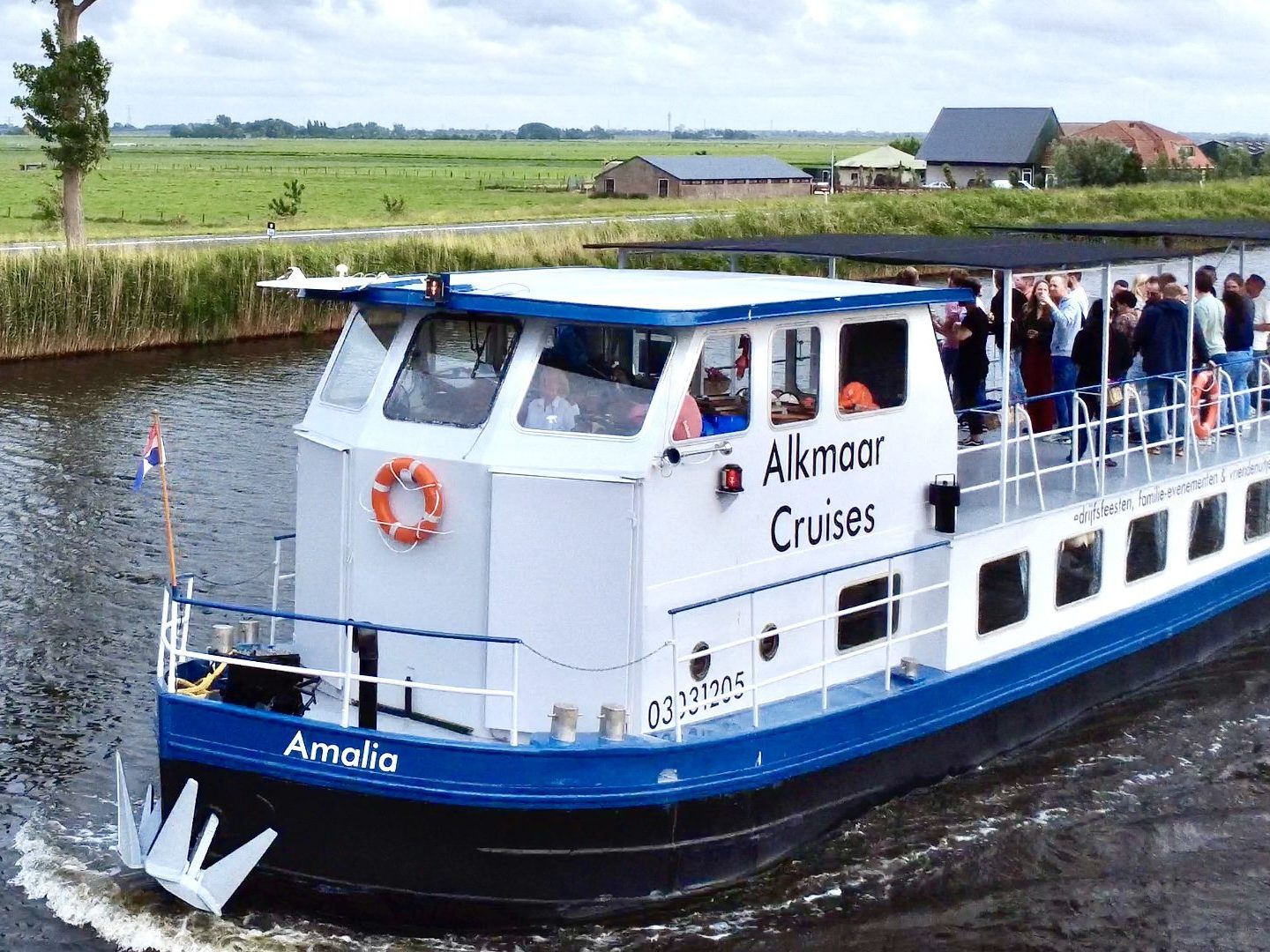 Boat labeled 'Alkmaar Cruises' sailing on a canal with people on board.