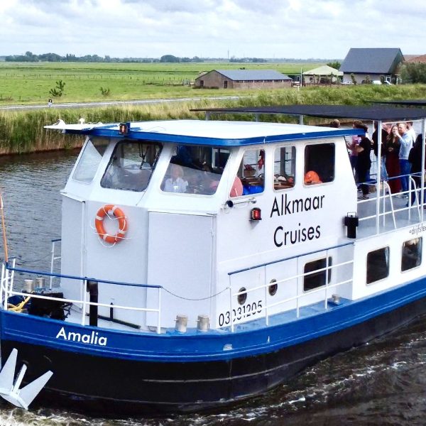 Boat labeled 'Alkmaar Cruises' sailing on a canal with people on board.