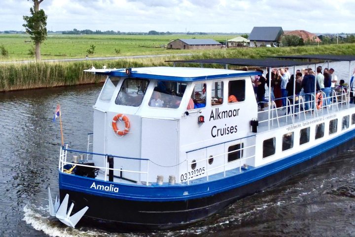 Boat labeled 'Alkmaar Cruises' sailing on a canal with people on board.