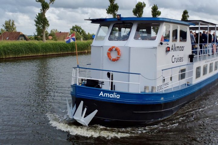 A blue and white passenger boat on a river with trees and a cloudy sky.