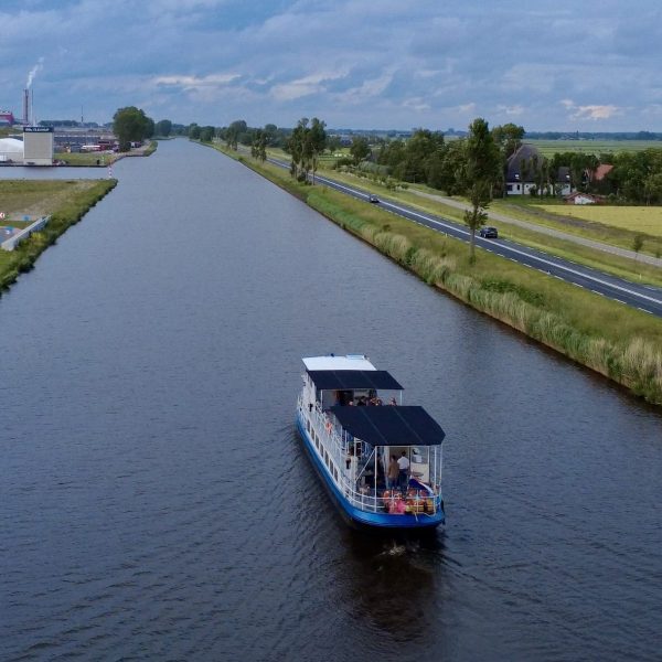 Boat on a canal with roads and fields on either side, wind turbines in the distance.