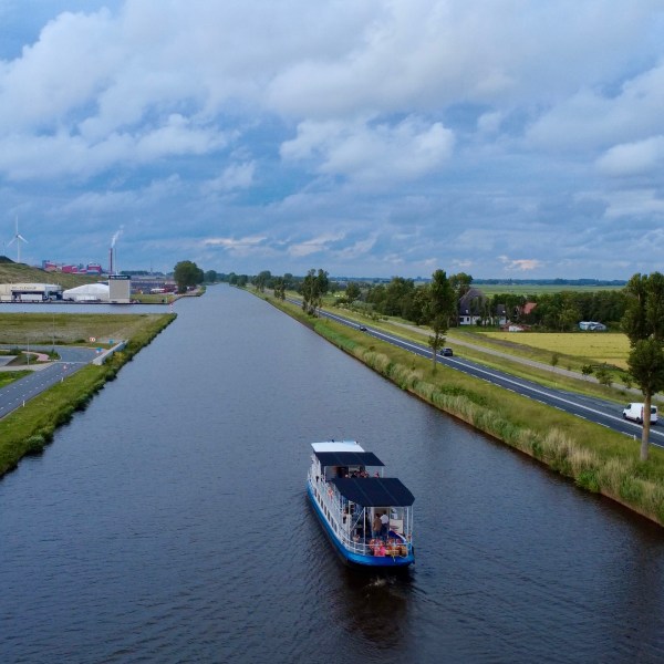 Boat on a canal with roads and fields on either side, wind turbines in the distance.