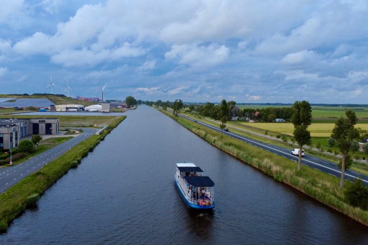 Boat on a canal with roads and fields on either side, wind turbines in the distance.